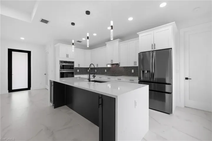 Kitchen featuring decorative backsplash, white cabinets, stainless steel appliances, light marble finish floors, and an island with sink