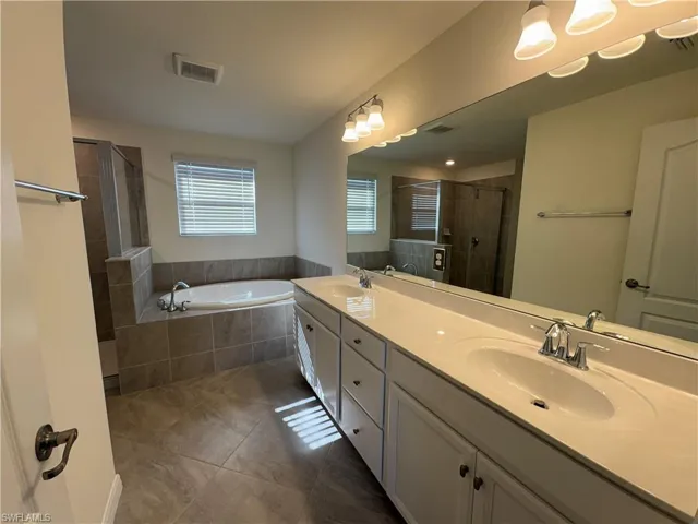 Full bath with double vanity, a shower stall, a bath, and dark tile patterned floors