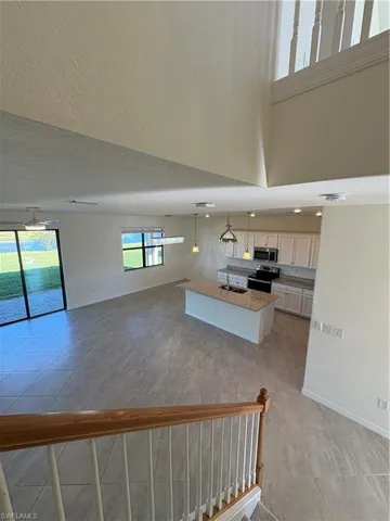 Kitchen with hanging light fixtures, a center island with sink, stove, open floor plan, and light stone counters