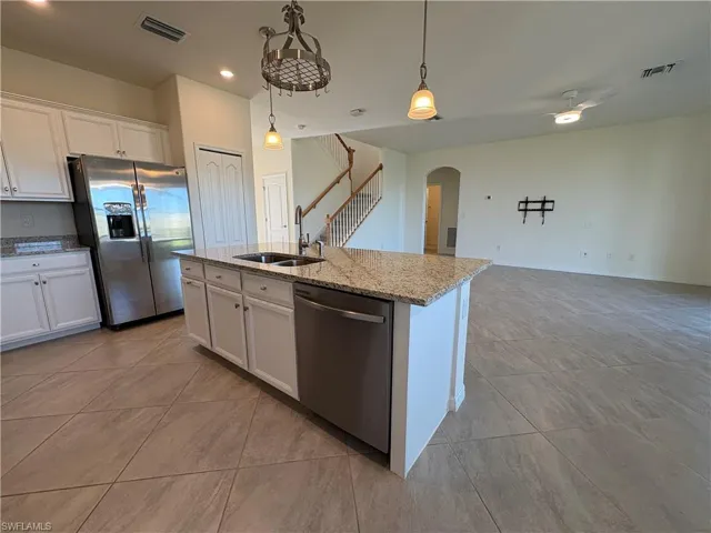 Kitchen featuring appliances with stainless steel finishes, white cabinetry, hanging light fixtures, a center island with sink, and light stone countertops