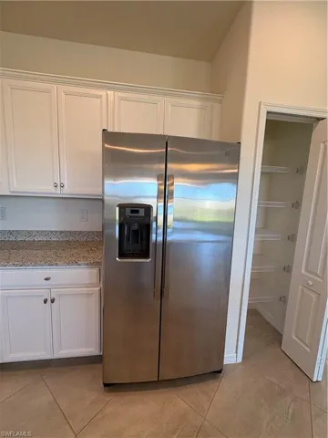 Kitchen with white cabinets, stainless steel refrigerator with ice dispenser, light tile patterned flooring, and light stone countertops