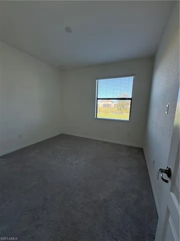Unfurnished room featuring dark colored carpet and a textured wall