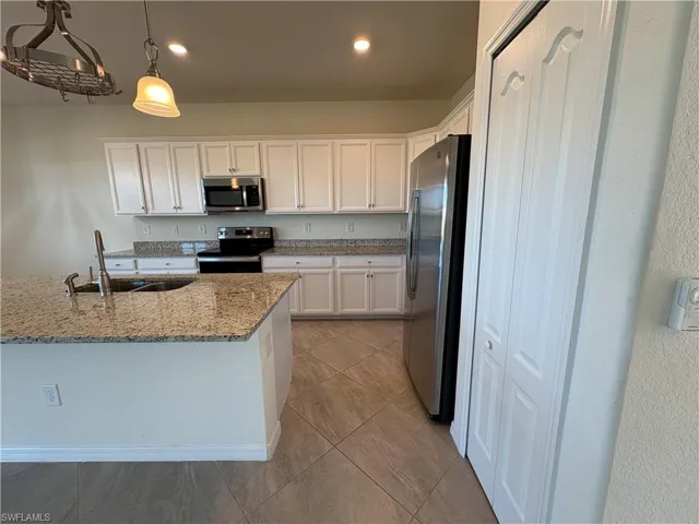 Kitchen with white cabinetry, appliances with stainless steel finishes, light stone counters, recessed lighting, and decorative light fixtures