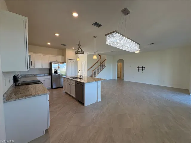 Kitchen featuring decorative light fixtures, recessed lighting, light stone counters, appliances with stainless steel finishes, and white cabinets