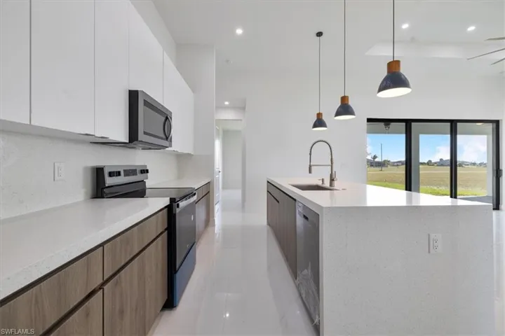 Kitchen with appliances with stainless steel finishes, modern cabinets, white cabinets, pendant lighting, and light stone countertops