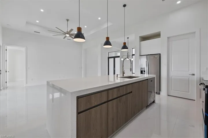 Kitchen featuring a tray ceiling, a large island, hanging light fixtures, stainless steel fridge with ice dispenser, and recessed lighting