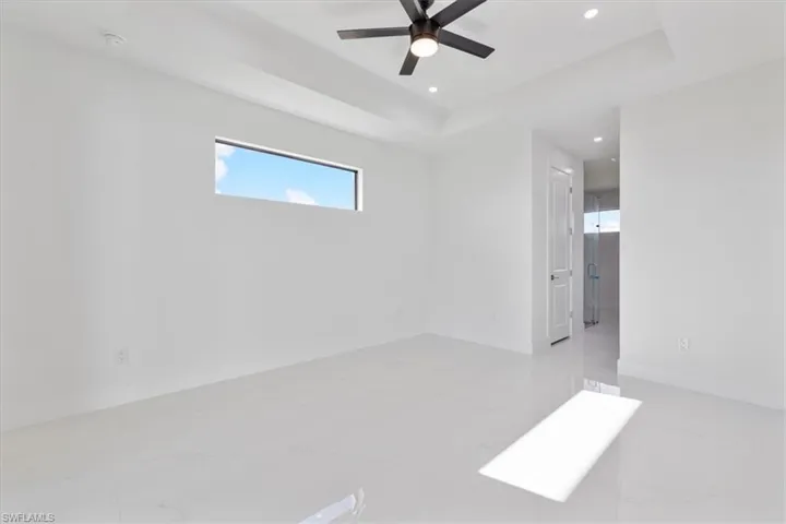 Spare room with a raised ceiling, recessed lighting, light marble finish floors, and ceiling fan