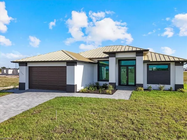 View of front of home with a metal roof, stucco siding, a standing seam roof, decorative driveway, and a front lawn