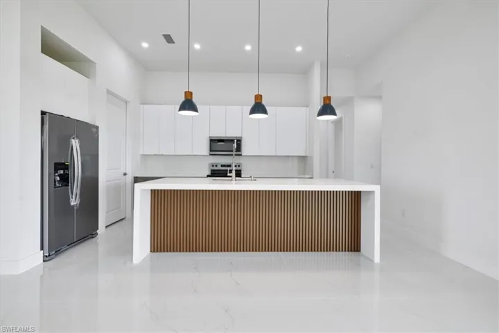 Kitchen featuring stainless steel appliances, an island with sink, white cabinetry, light stone countertops, and recessed lighting