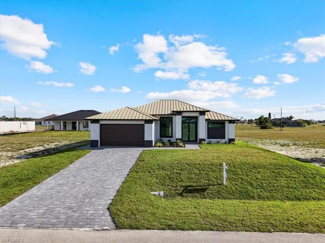 View of front facade with a metal roof, decorative driveway, a front lawn, a standing seam roof, and a garage
