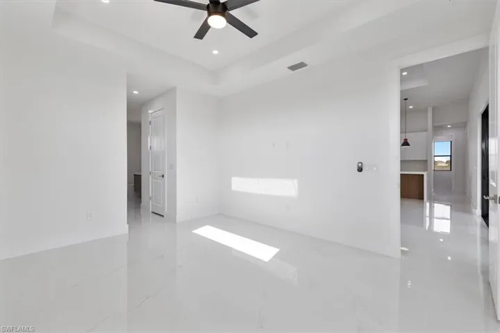 Empty room featuring a tray ceiling, recessed lighting, light marble finish flooring, and a ceiling fan