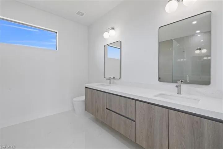 Full bath with double vanity, light marble finish floors, and a shower stall
