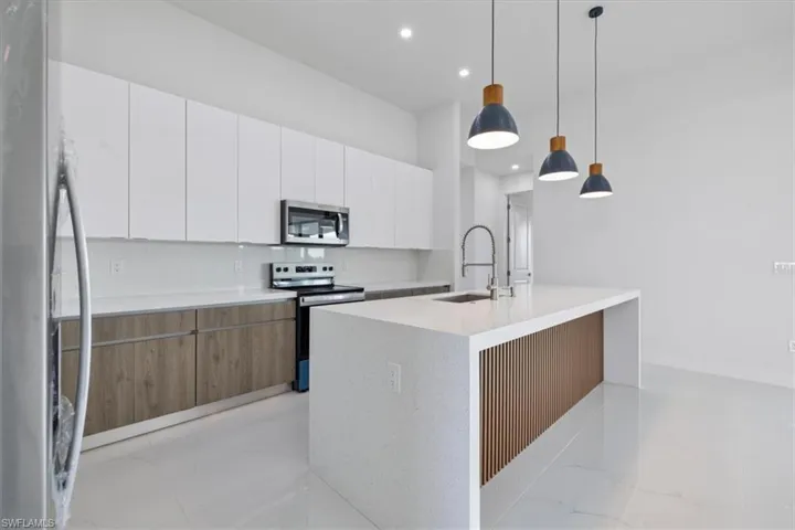 Kitchen with modern cabinets, stainless steel appliances, decorative light fixtures, white cabinets, and light stone countertops