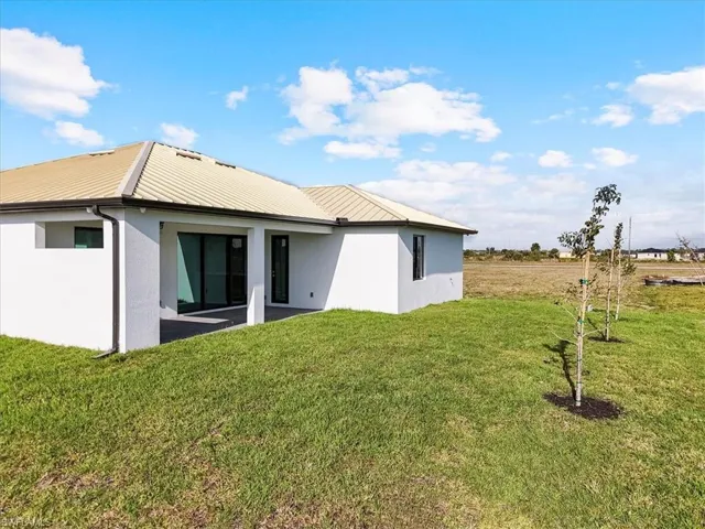 Rear view of house with stucco siding, a yard, a metal roof, and a patio