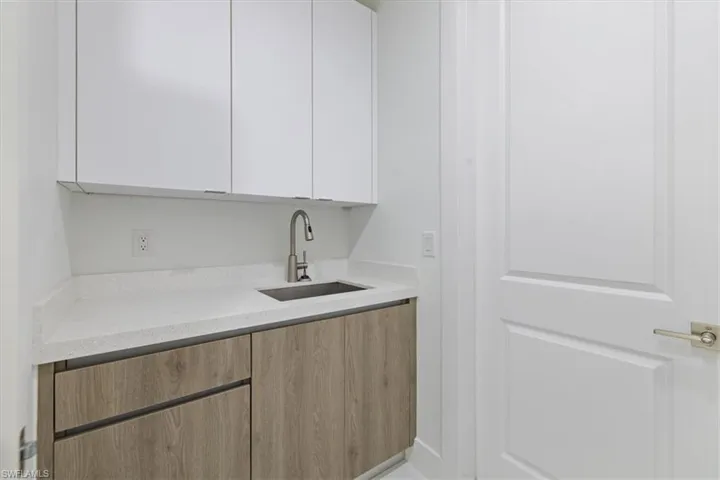 Bar area with modern cabinets, light stone counters, white cabinetry, and light brown cabinets