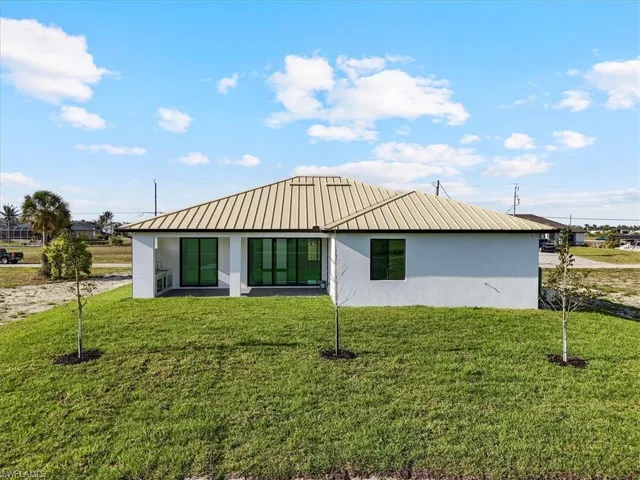 View of front of house with stucco siding, a front lawn, and a metal roof