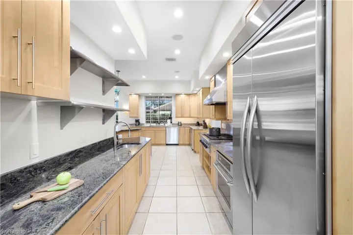 Kitchen featuring stainless steel appliances, open shelves, a sink, light brown cabinets, and dark stone counters