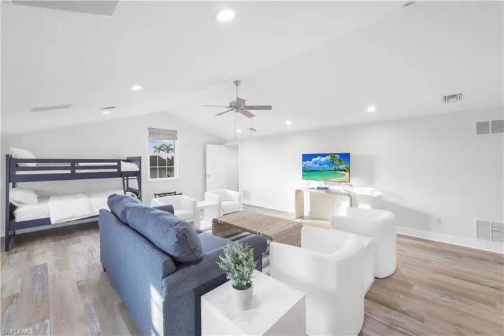Living area featuring wood finished floors, vaulted ceiling, a ceiling fan, baseboards, and recessed lighting