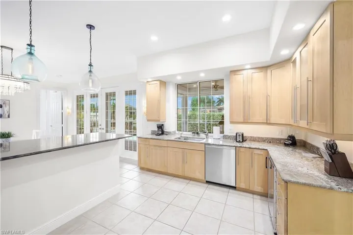 Kitchen featuring stainless steel dishwasher, light brown cabinetry, a sink, light tile patterned floors, and light stone countertops