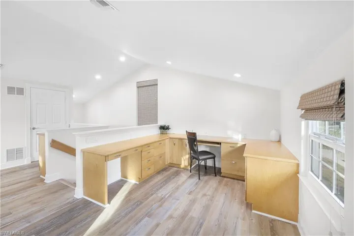 Office space with built in desk, vaulted ceiling, light wood finished floors, and recessed lighting