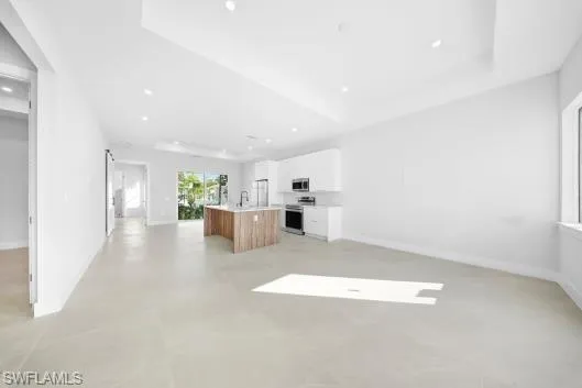 Kitchen featuring open floor plan, light countertops, a center island with sink, stainless steel appliances, and dual tone cabinetry