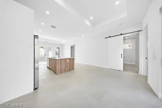 Unfurnished living room featuring a barn door, a raised ceiling, recessed lighting, and concrete floors