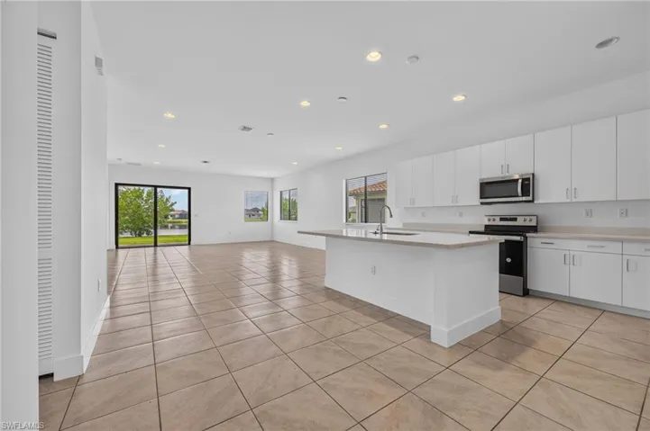 Open-concept living area featuring a kitchen island with sink, white cabinetry, integrated stainless steel appliances, and tile flooring