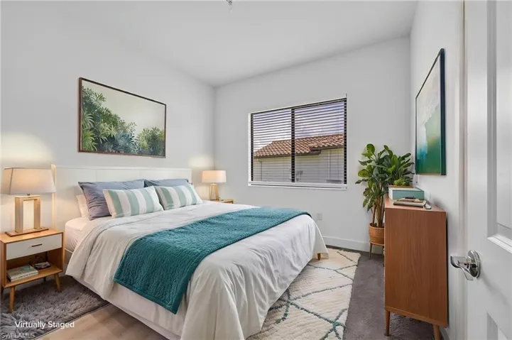 Light wood-finish flooring, white walls, horizontal window blinds, white interior door, and a low-pile carpeted area
