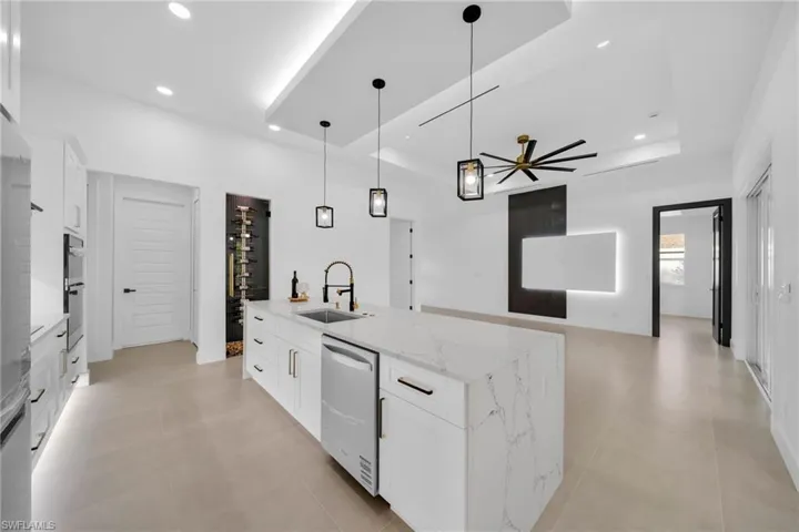 Kitchen with a center island with sink, a sink, appliances with stainless steel finishes, white cabinets, and a raised ceiling