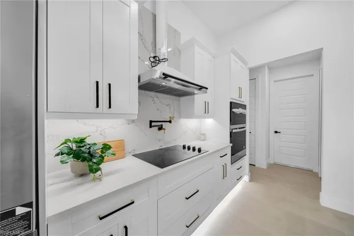 Kitchen featuring backsplash, wall chimney exhaust hood, white cabinets, light countertops, and black electric stovetop