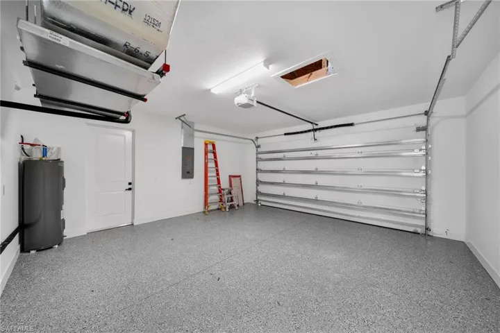 Garage featuring water heater, baseboards, a garage door opener, and electric panel