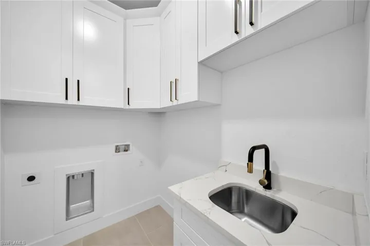 Clothes washing area with light tile patterned floors, cabinet space, electric dryer hookup, washer hookup, and a sink