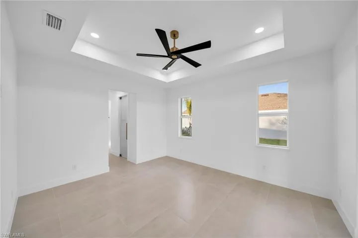Empty room with a tray ceiling, baseboards, visible vents, and a wealth of natural light