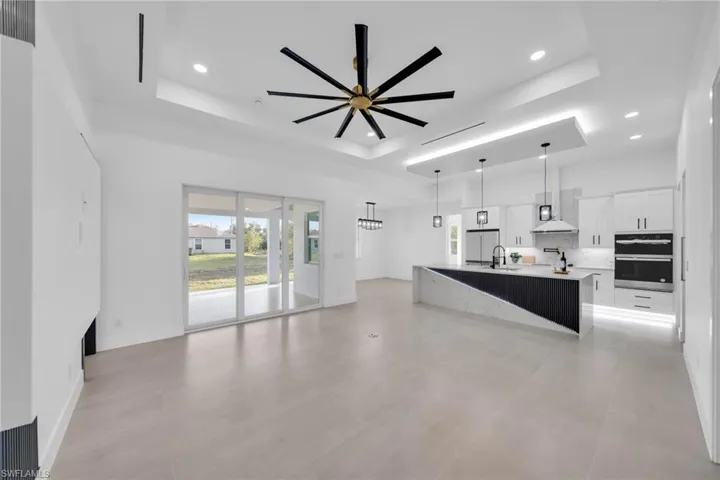 Unfurnished living room with baseboards, recessed lighting, ceiling fan, a sink, and a raised ceiling