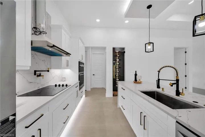 Kitchen featuring dishwashing machine, black electric cooktop, a sink, wall chimney exhaust hood, and backsplash