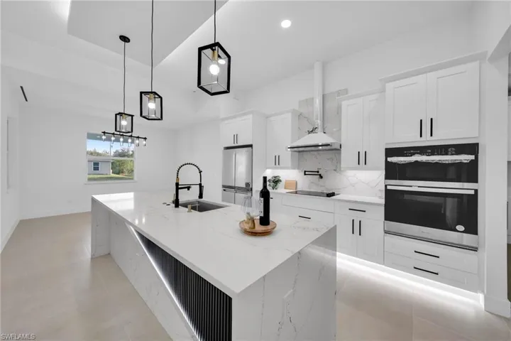 Kitchen with freestanding refrigerator, a sink, wall chimney exhaust hood, black electric cooktop, and backsplash