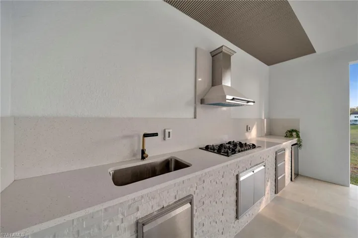 Kitchen featuring gas cooktop, light countertops, wall chimney exhaust hood, and a sink