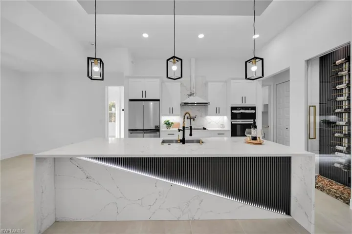 Kitchen featuring a large island, double wall oven, a sink, white cabinetry, and stainless steel fridge