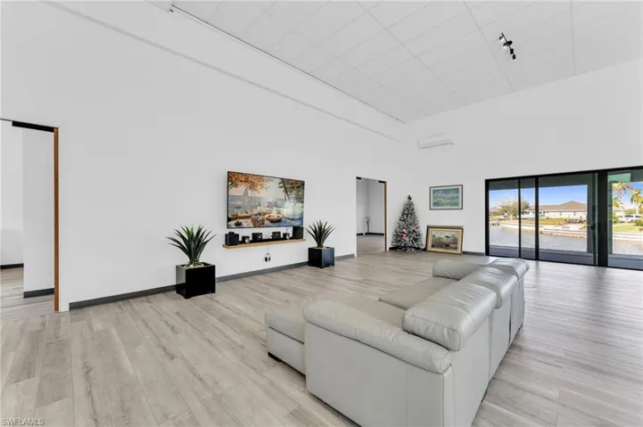 Living area with a towering ceiling, light wood-style flooring, and an AC wall unit