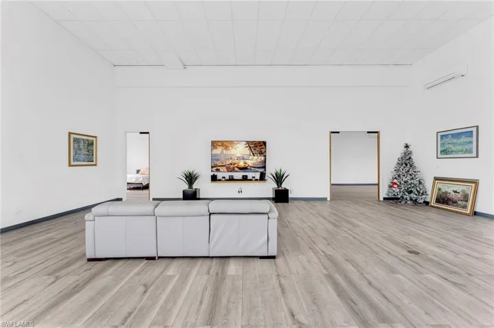 Living room with a high ceiling, a wall mounted air conditioner, and light wood-style floors