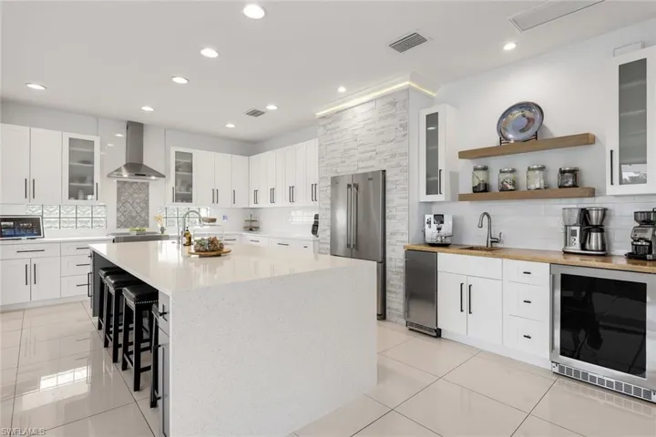 Spacious kitchen featuring an expansive island with seating, white shaker-style cabinetry with black hardware, stainless steel appliances, and recessed lighting