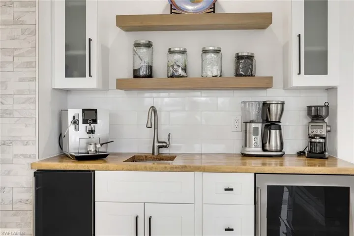 Wood-finish countertop with an undermount sink, white subway tile backsplash, and two floating wood-finish shelves