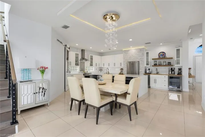 Open-concept living space with large format tile flooring, a contemporary chandelier, recessed ceiling lighting, a kitchen island with seating, and stainless steel appliances