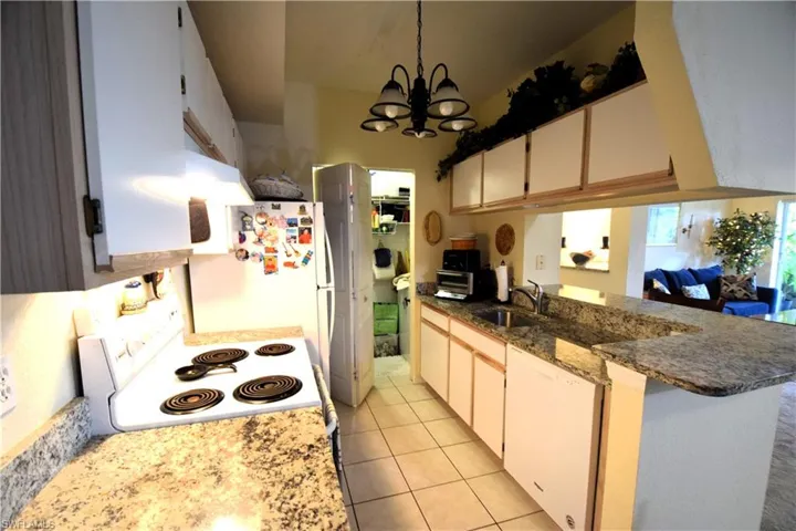 Kitchen featuring white appliances, a sink, a peninsula, a chandelier, and light tile patterned flooring
