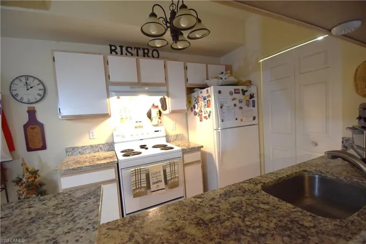 Kitchen featuring white appliances, under cabinet range hood, white cabinetry, light stone counters, and a chandelier