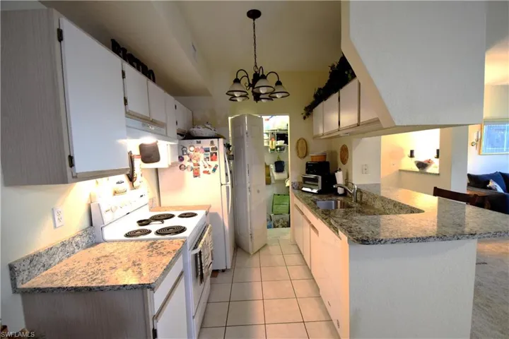 Kitchen featuring white appliances, a sink, a chandelier, a peninsula, and under cabinet range hood