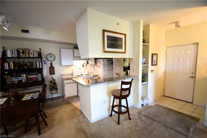 Kitchen with freestanding refrigerator, stove, a peninsula, white cabinetry, and light stone countertops