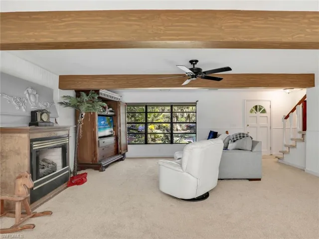Living room with beam ceiling, carpet flooring, a fireplace, stairway, and a ceiling fan