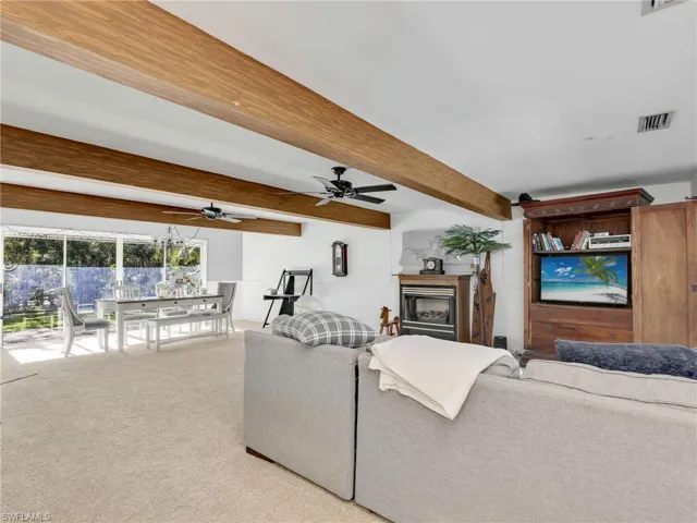 Living area featuring light colored carpet, beamed ceiling, and a glass covered fireplace