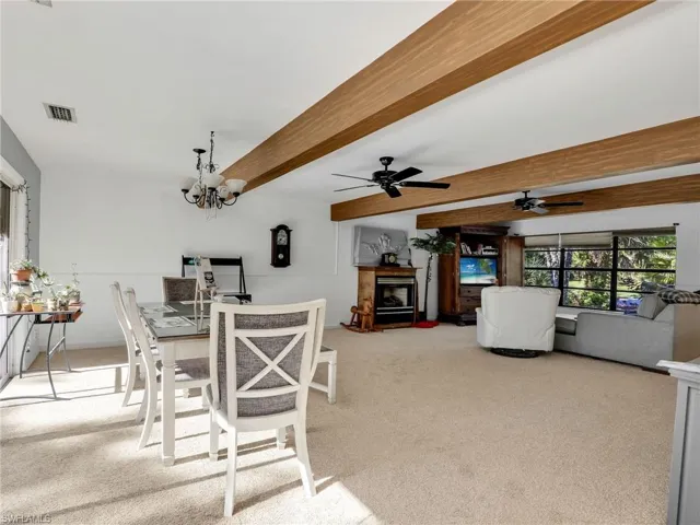 Dining room with beamed ceiling, light carpet, a ceiling fan, and a chandelier